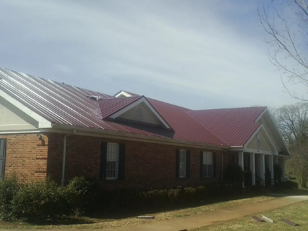 Red metal roof with gabled entries on a long brick building, from a Hail Damage Roof Repair job in Eltopia