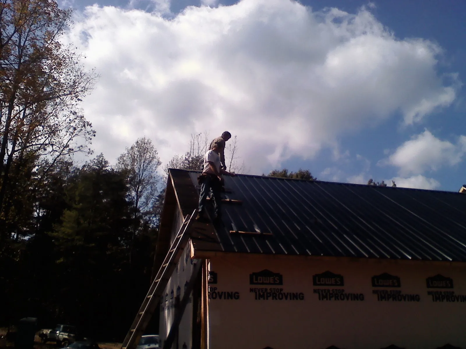 Roofer fastening dark metal panels high against a cloudy sky, from a Roof Inspection job in Eltopia